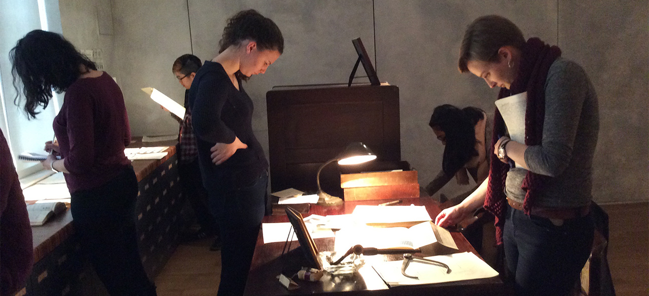 Students look at paper records spread across a table. 