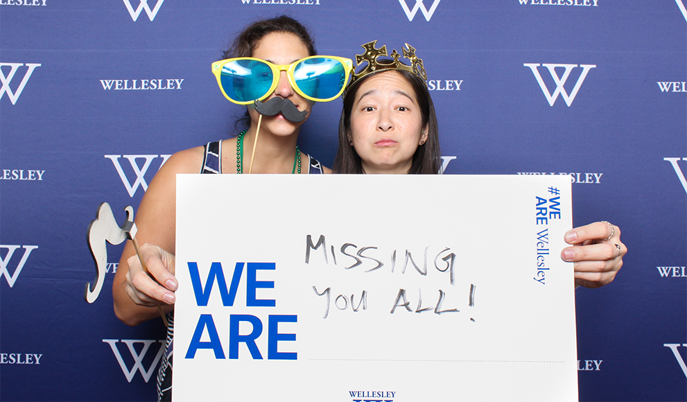 Alumnae hold a sign during the reunion photo both reading "We Are Missing You All"