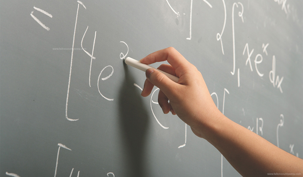 Hand writes equations in chalk on a green chalkboard