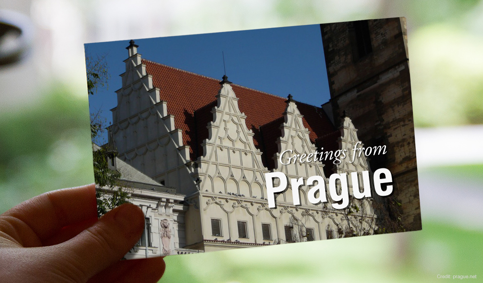 Hand holds a postcard that reads "Greetings from Prague"