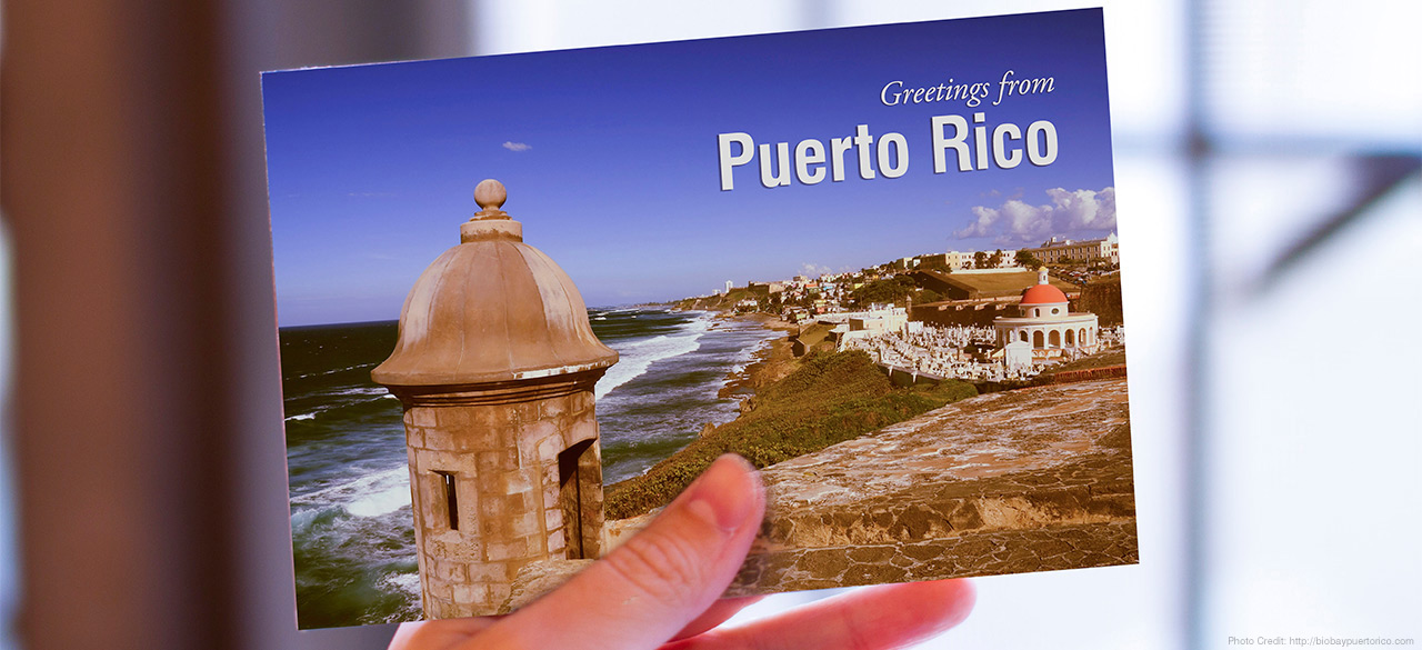 Hand holds a postcard that reads "Greetings from Puerto Rico"