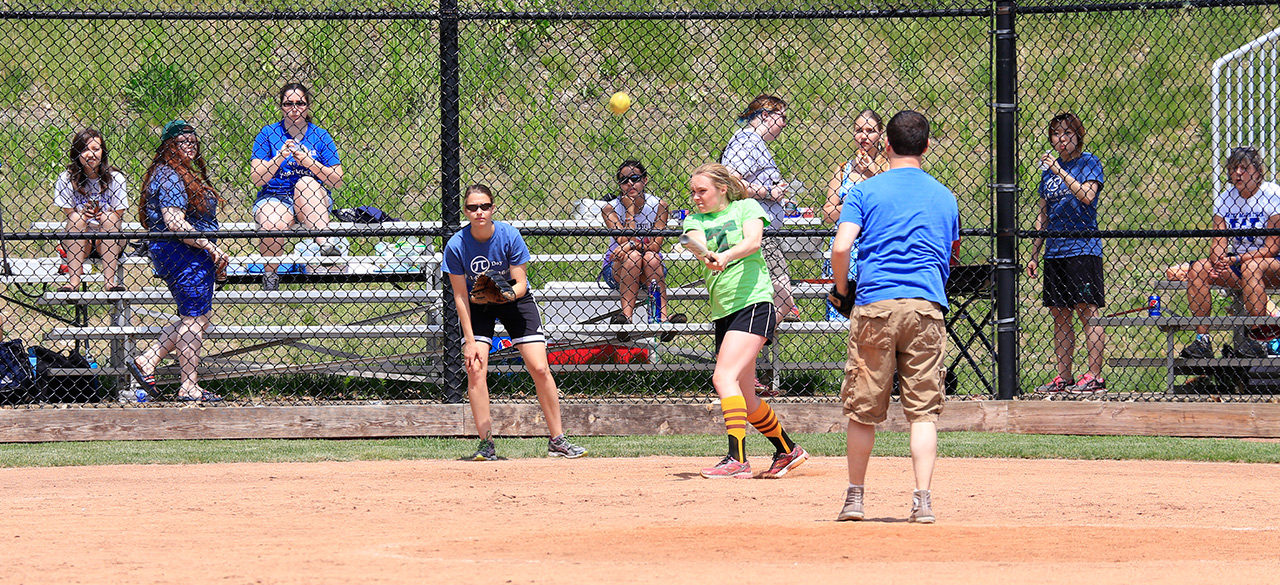 Fans look on from the stands as a softball player hits the ball