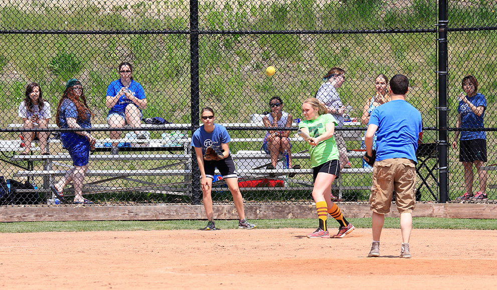Fans look on from the stands as a softball player hits the ball