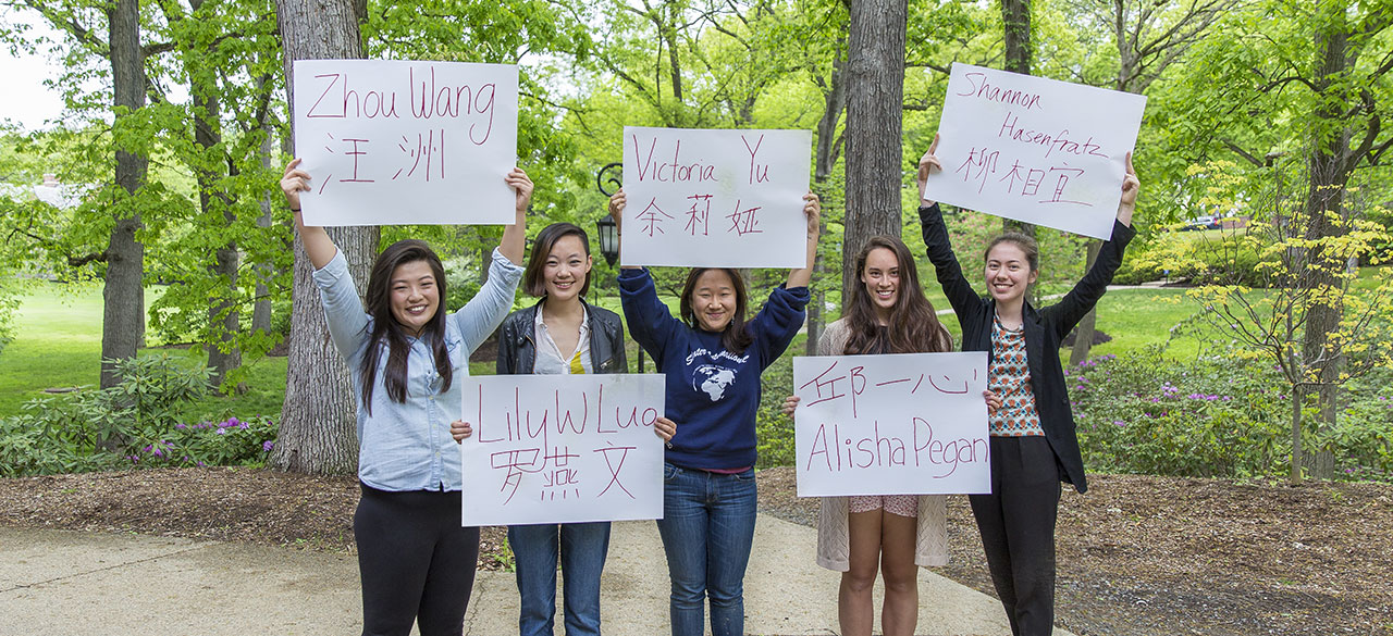 Students hold signs with their names written in English and an alternative alphabet.