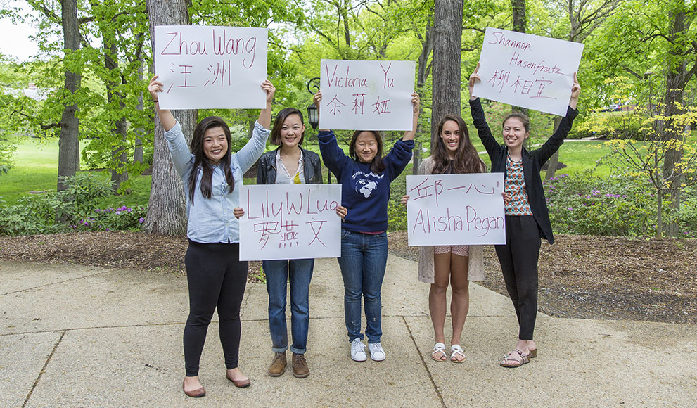 Students hold signs with their names written in English and an alternative alphabet.