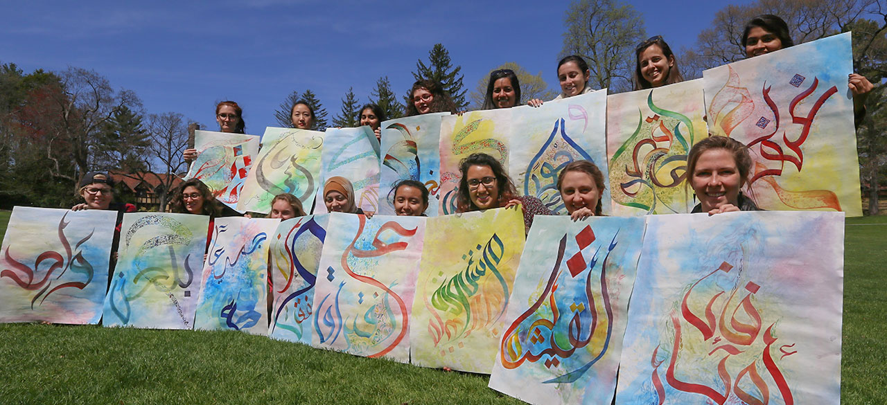 Students hold art from a calligraphy project exploring Arabic letters