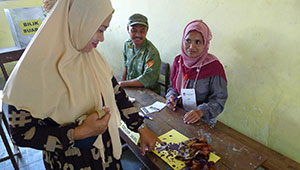 woman in headscarf dips finger in ink at a table in Indonesian voting place