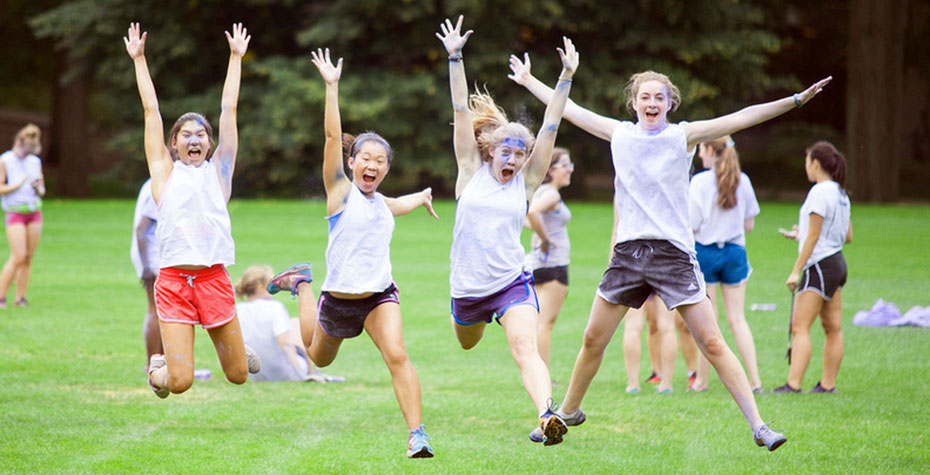 four students leaping and laughing, splattered with purple paint