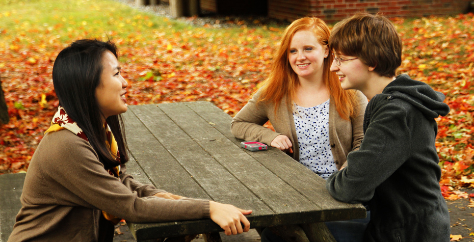 Tran, Altenhof-Long, and Peeler chat at picnic table with yellow leaves in background