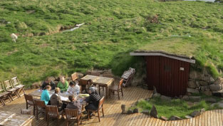 students and lecturer meet at a table outdoors in front of underground house