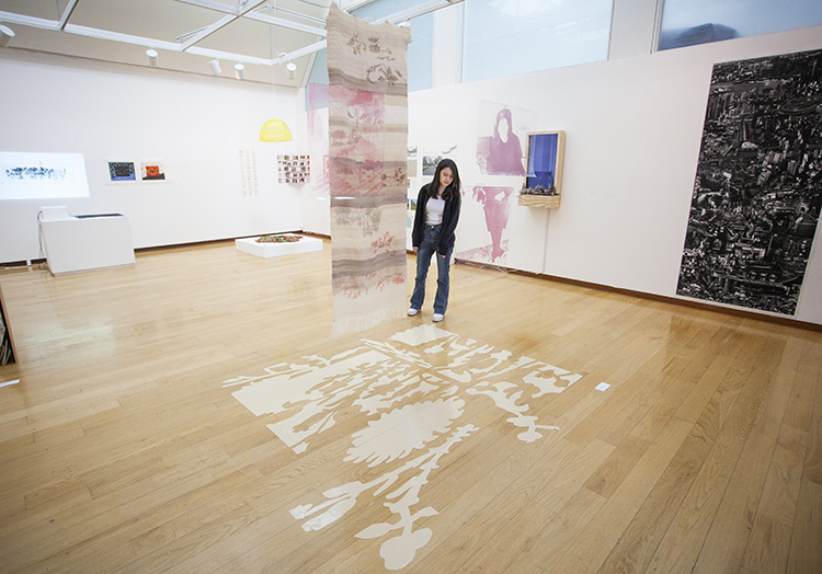 a person looking at a hanging textile and hanging printed transparencies above a patterned vinyl section of flooring in a gallery