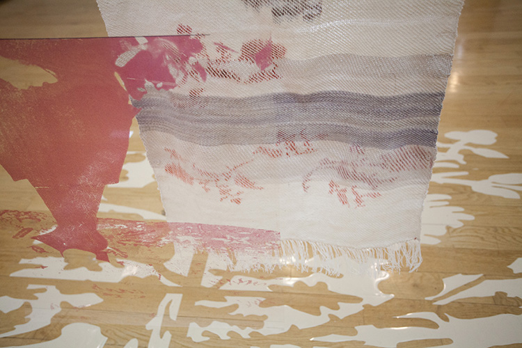 looking down at a hanging cream and purple striped textile, through several layers of hanging transparencies printed with pink overlay