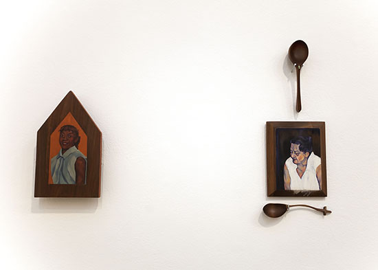 a house shaped wood panel with portrait of woman at left, rectangular wood panel with portrait of older woman at right with vertical thin-stemmed spoon above and horizontal thin-stemmed spoon below