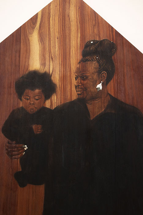 close up on a dark wood panel with pyrography drawing of woman holding a child, with inlaid mother of pearl earring and fingernails