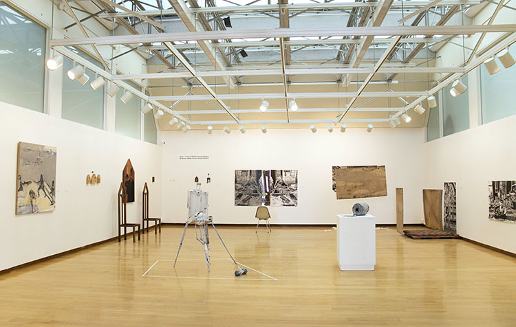 gallery with white walls and wood floor, installed with various diverse wall works, freestanding sculptures, and sculptures on pedestals
