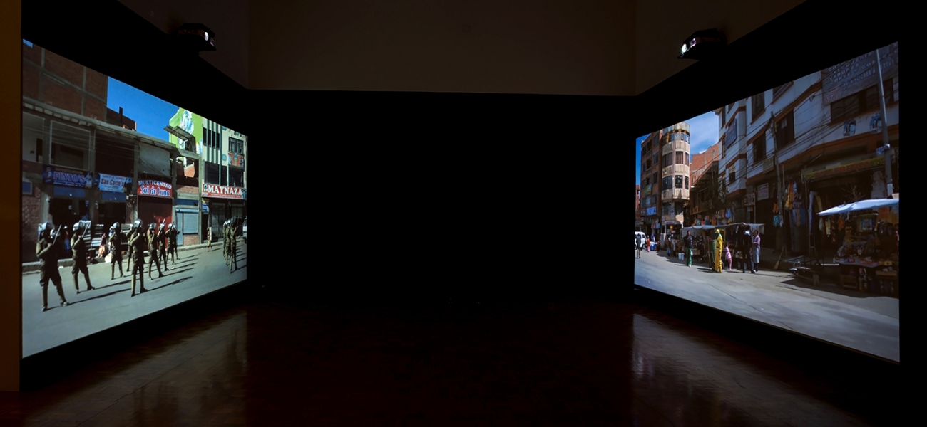 photo of video installation, two screens across a dark room from each other showing street scenes