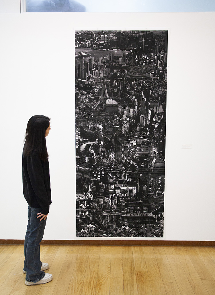 a person standing to the side of a very tall black and white composite photographic print of merged cityscapes