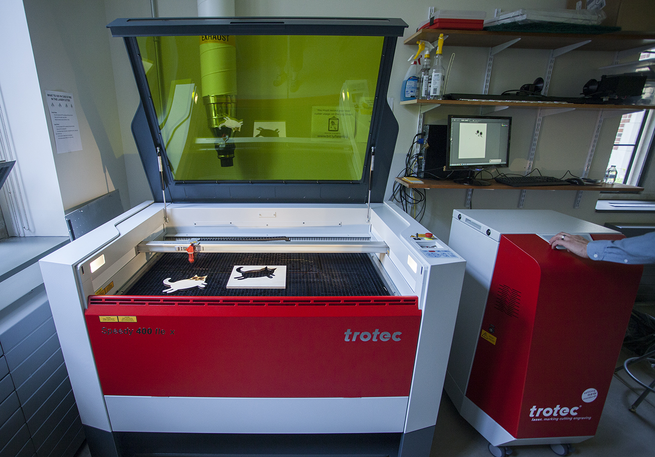 laser cutter with green glass lid open showing black cutter bed with small wood cat cut out