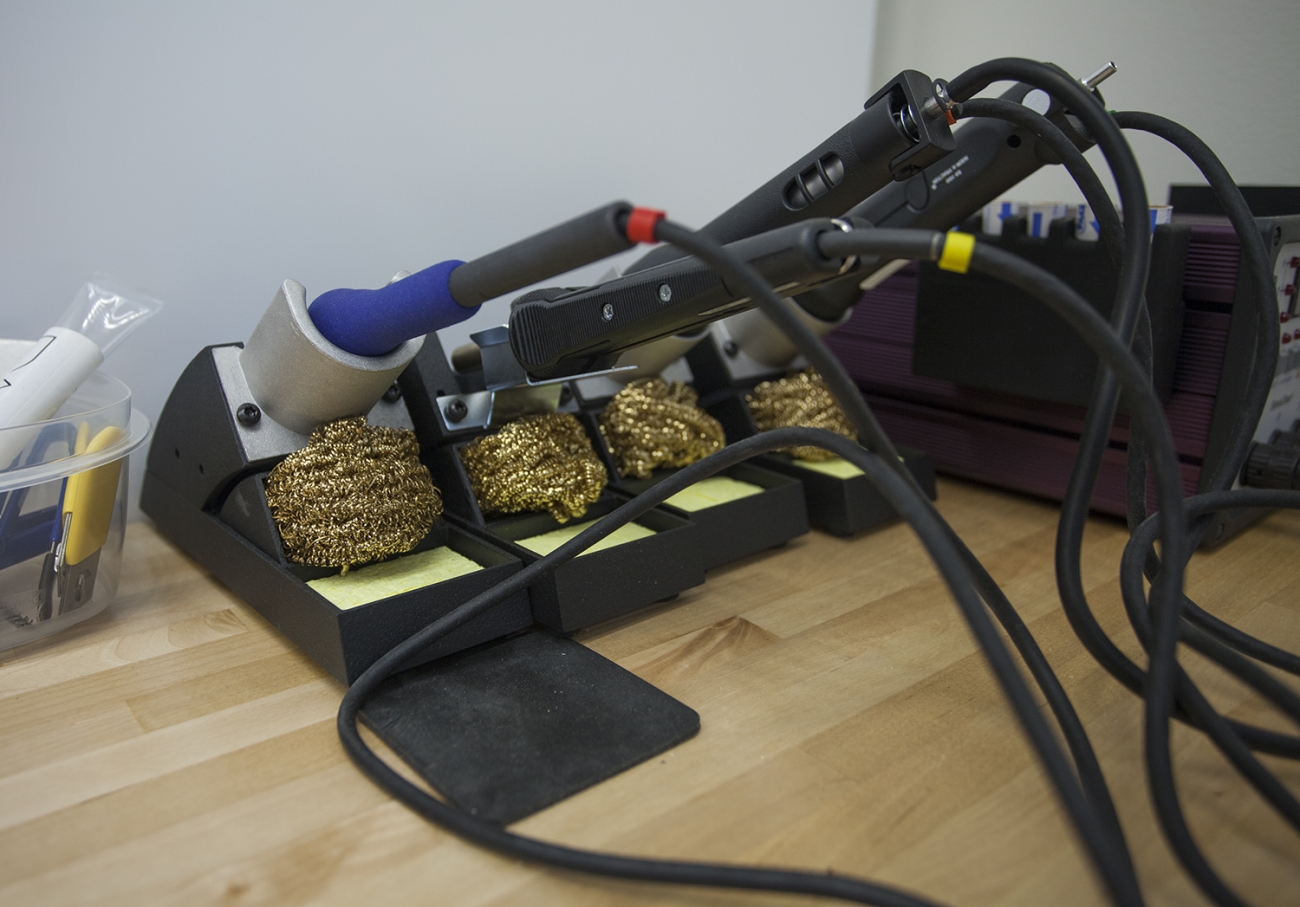 soldering irons lined up in holders with wires and brass wire cleaner balls