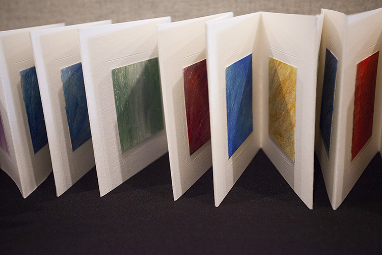 close up on a section of an accordion book; each page has an incised square frame in the center, and in the center of each frame is a differently colored square