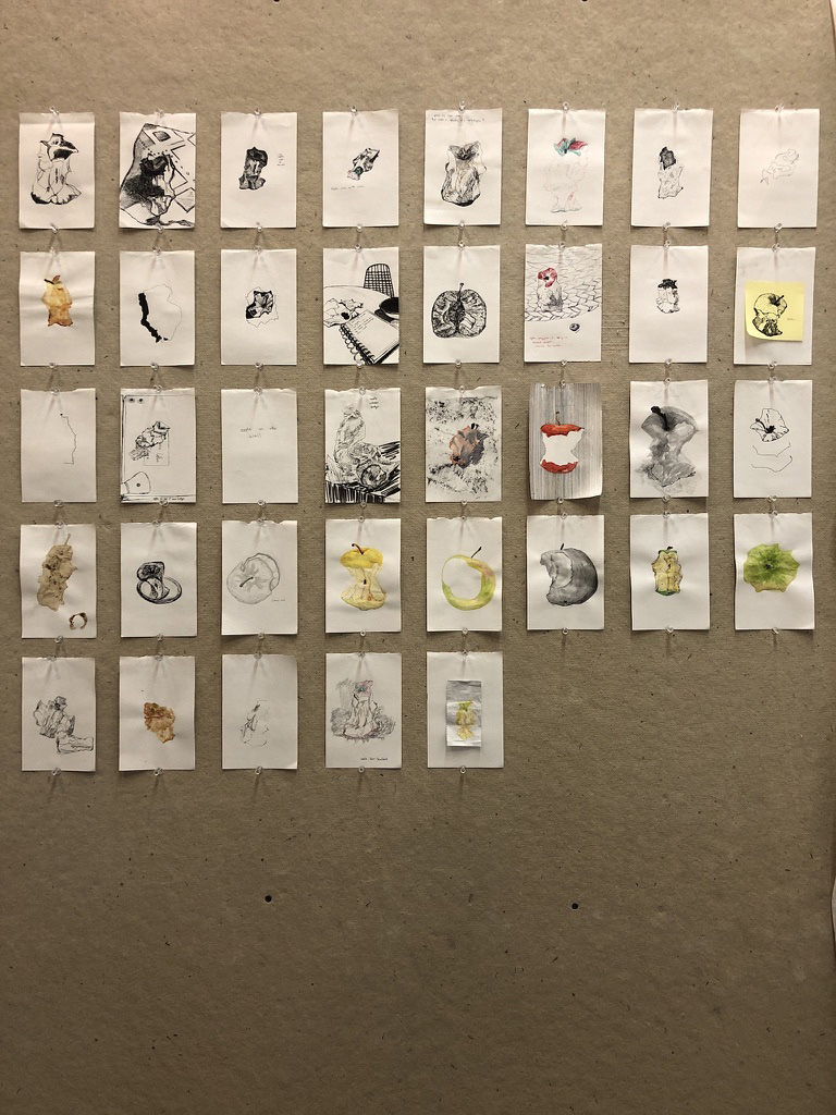 grid of small paintings on paper of apples in various states of completeness on tan wall