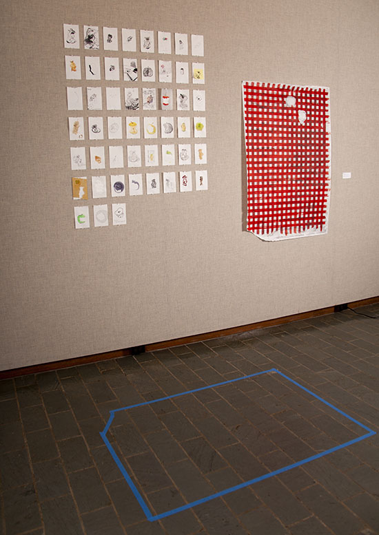 on a grayish fabric wall, a large grid arrangement of small drawings, with a red and white checked painting on paper to its right. On the floor is the shape of the red and white painting marked out in blue tape.
