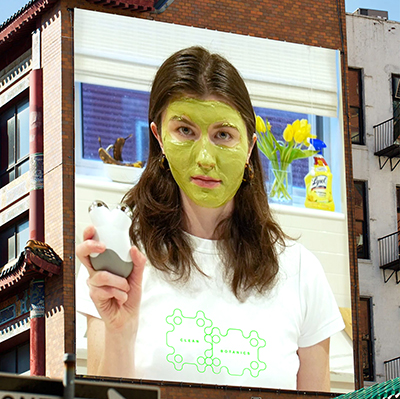 mocked up billboard on side of building showing woman with green cream all over face, holding white and silver device