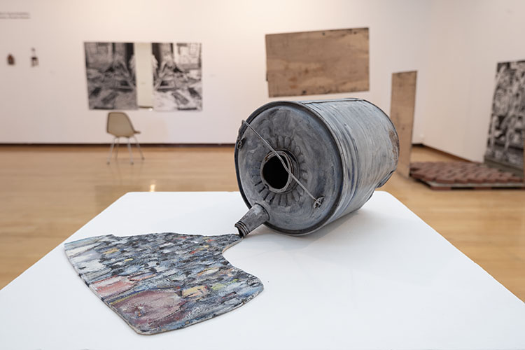 painted oil can lying on its side, with board spill painted with an expressionistic crowd scene