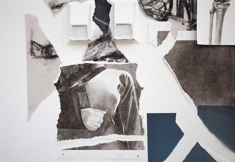 close-up on wall mounted collage of ripped pieces of charcoal drawings, one showing an arm in a sling