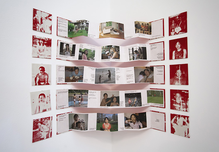 5 small accordion photo books stretched across the corner of a gallery; red and white pixelated photos are attached to the wall at the ends of each book