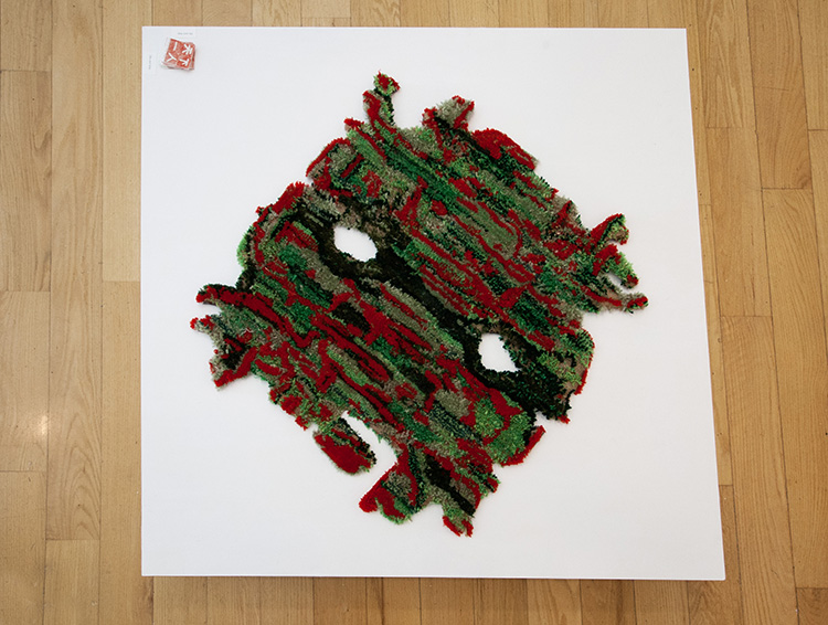 top down view of irregular green and red rug on a square white pedestal