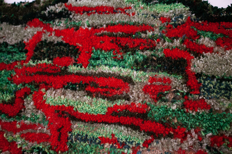 close up on the surface of a hand-tufted rug in bright red and shades of green, white, and brown