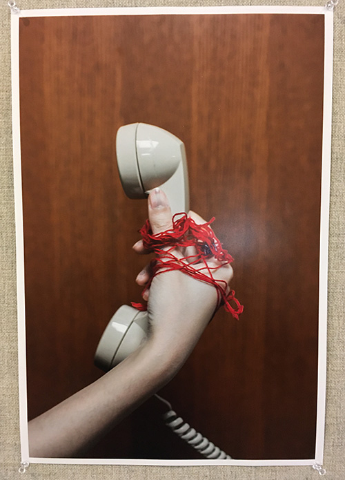 photograph of hand holding pale phone, red string around hand, dark wood background