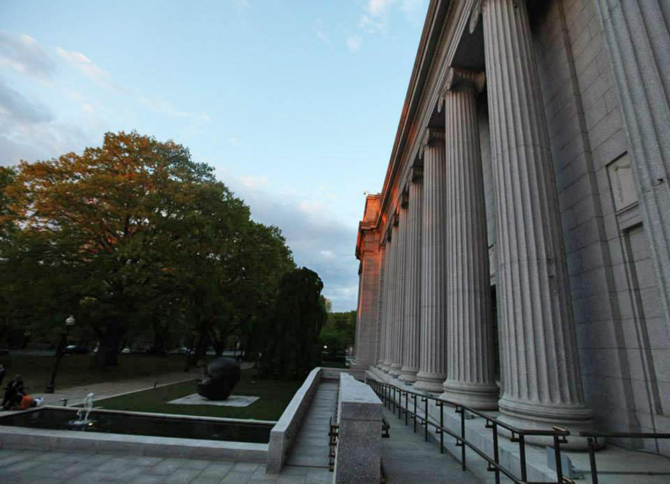 photo of the front facade of the Museum of Fine Arts Boston showing gray stone columns, lawn, sculpture of a baby's head