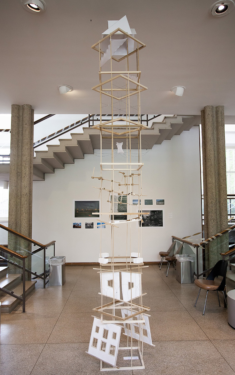 a spindly wooden tower in a gallery space with stairs and columns in the background