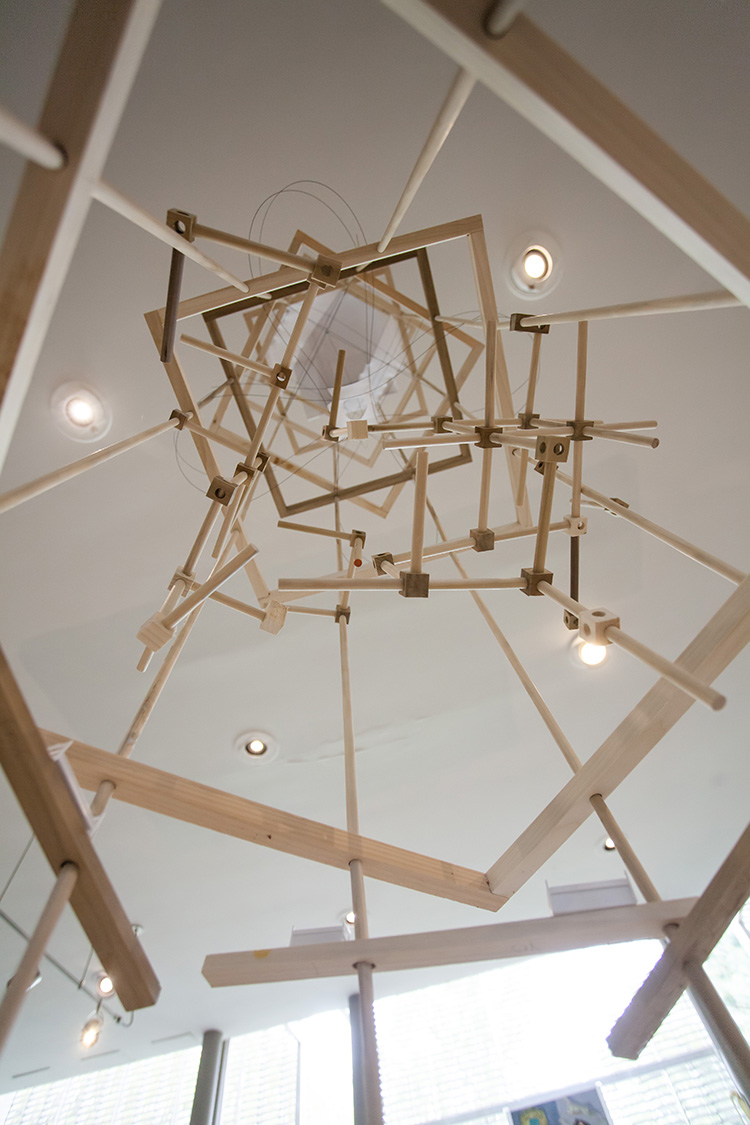 view looking up through the center of a tall structure made of wooden dowels attached in all sorts of configurations