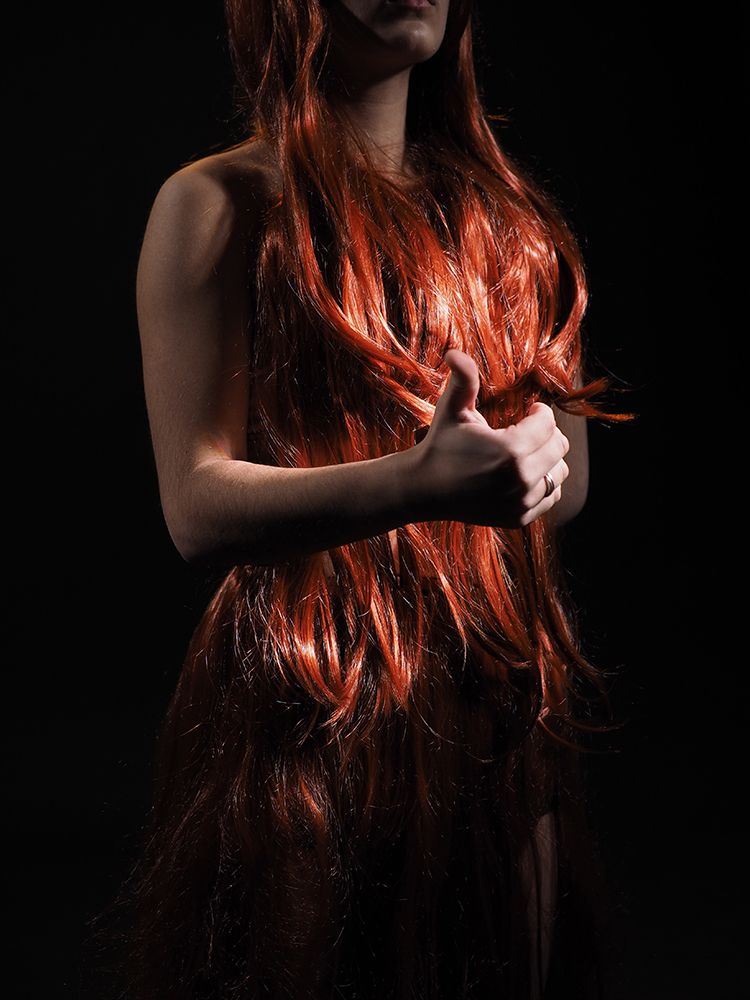 person standing on black background, body covered with long red hair, one hand held in front making a thumbs up gesture