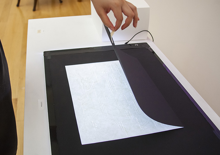 person's hand delicately lifting the cover of a flat light box