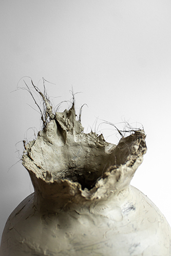 close up on mouth of grayish clay vessel with dark hair embedded in and coming out of the clay