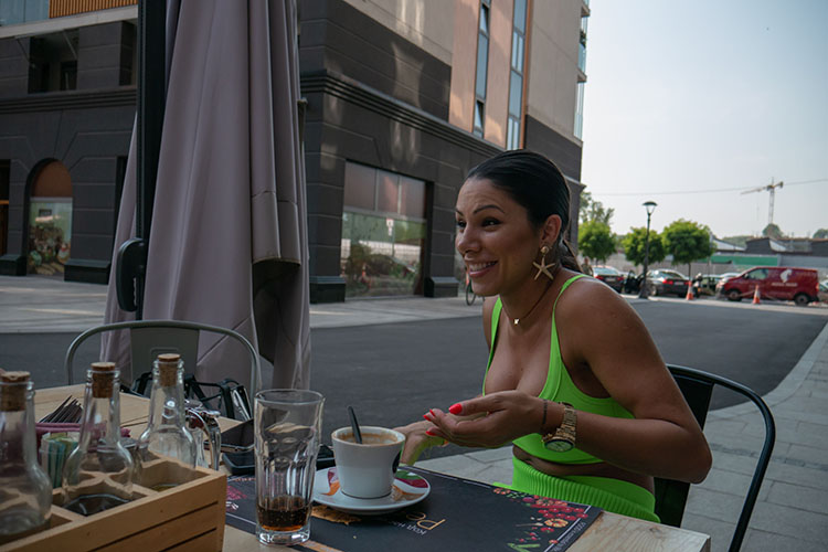 woman in lime green tank top and starfish earrings sitting at outdoor cafe table