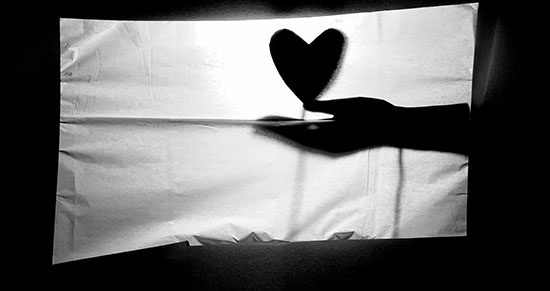 black hand silhouette with cartoon heart projected shadow puppet style on a white sheet