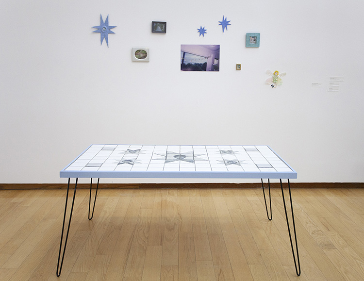 white tile surface table with light blue trim and black hairpin legs in a gallery with small photos and 8 pointed blue stars on the wall behind