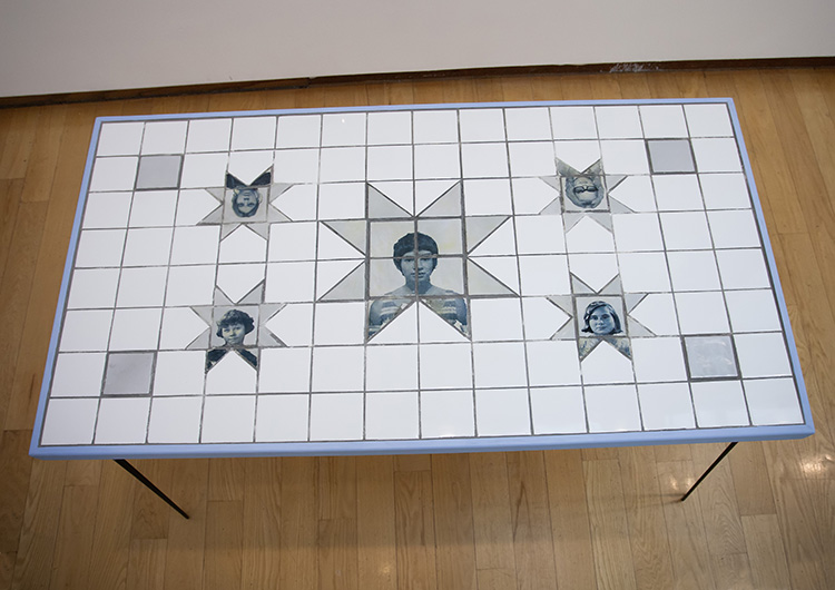 looking down at the surface of a white tiled table with 8 pointed stars with blue-toned portraits of people scattered around the surface