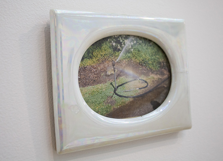 angled close up of an iridescent puffy white frame with oval opening showing a photo of a sprinkler with rainbow