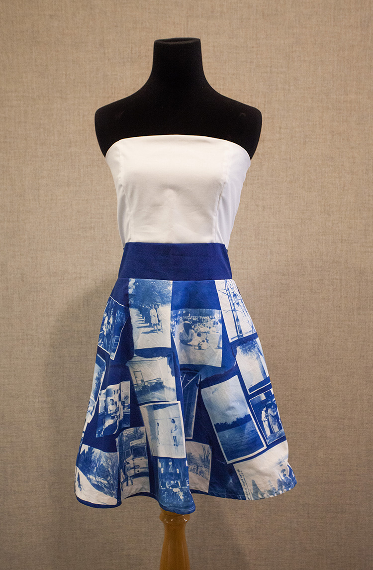 dress with a white strapless bodice and a blue and white skirt printed with cyanotypes on a black dress form in front of a gray fabric wall