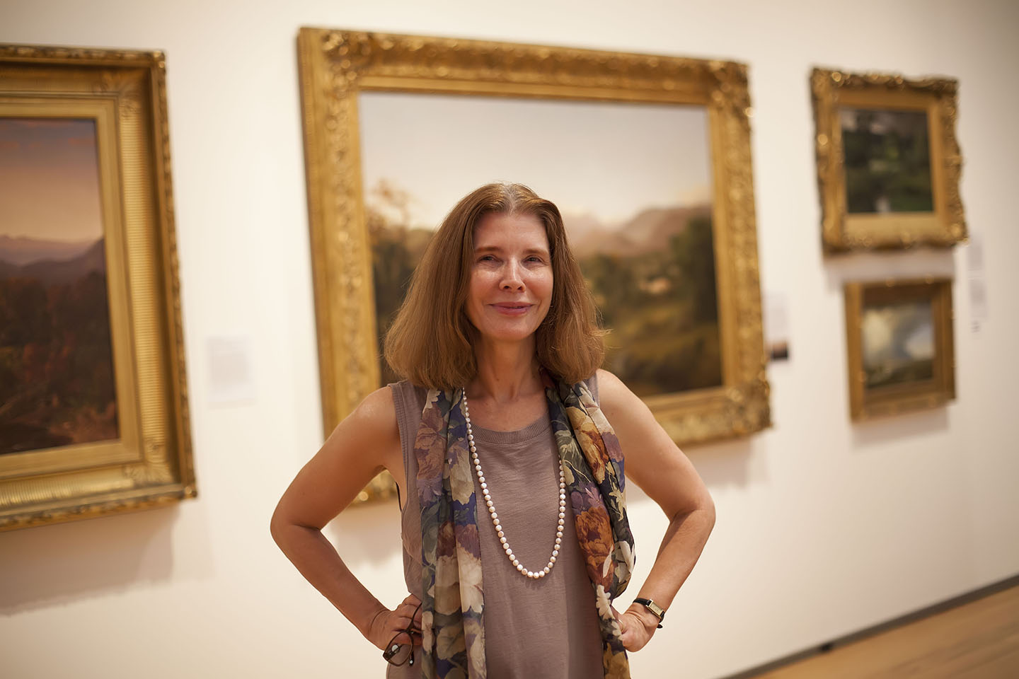 Rebecca Bedell standing in front of gilt-framed landscape paintings