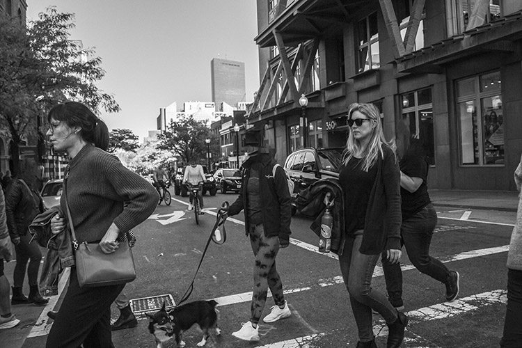 black and white photo of people crossing a busy city street, some with heads removed from the image