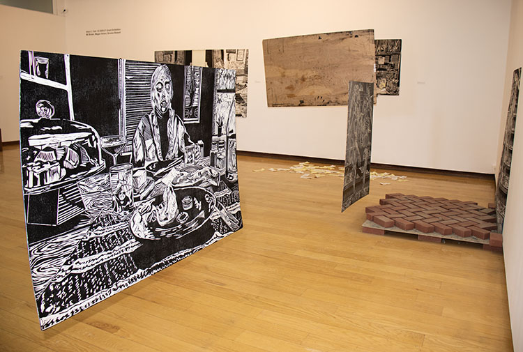 large black and white inked board showing person sitting at laden table, hanging in the air