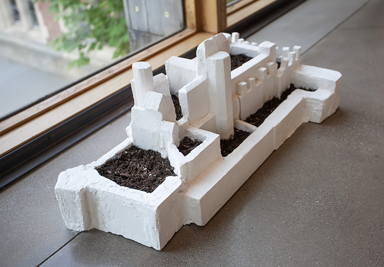 white walled fort model filled with dark dirt, sitting on the floor with windows behind