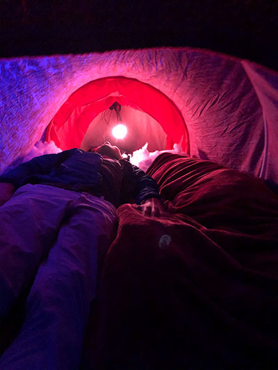 figure lying in pink and red fabric tunnel space lit from single light by their head